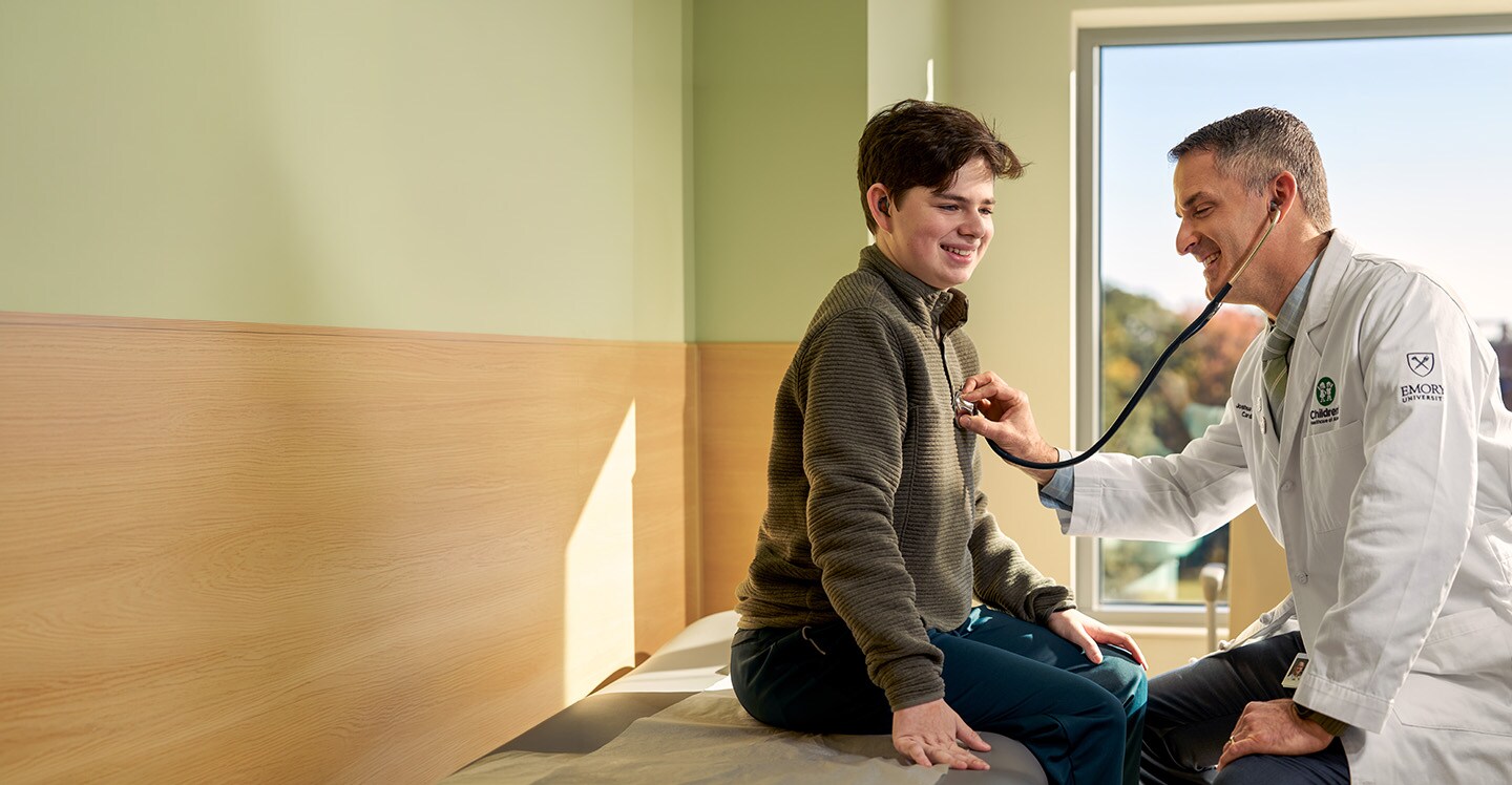 A heart doctor smiling as he listens to a teenager's heartbeat
