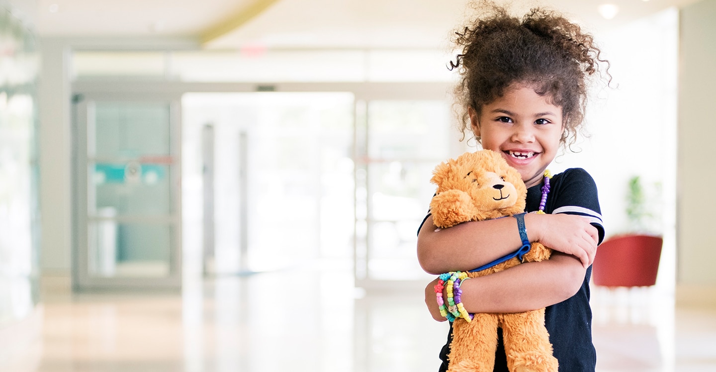 Girl patient hugging a teddy bear in lobby of pediatric hospital