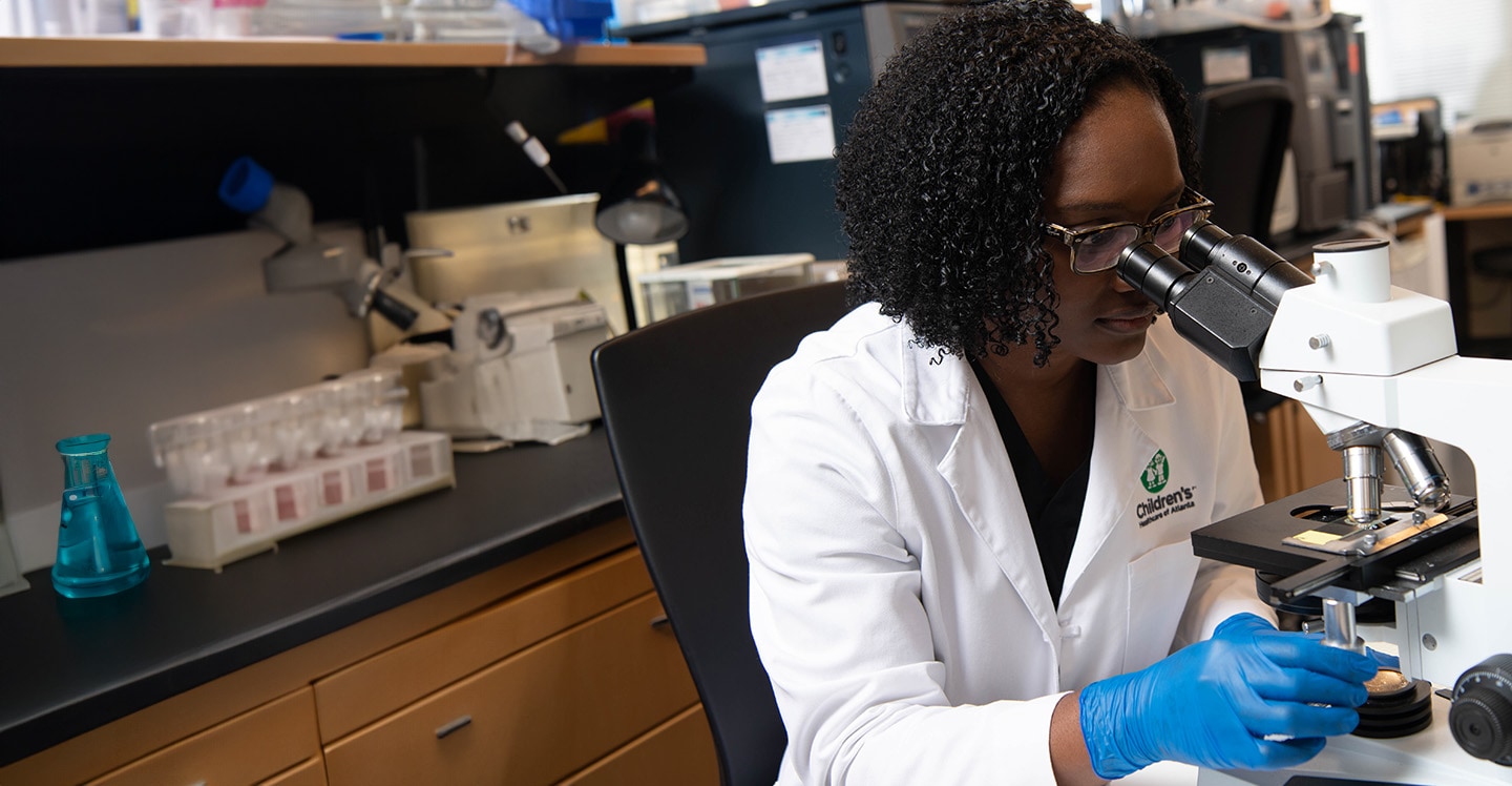 Pediatric research analyst viewing samples through a microscope.