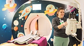 Healthcare provider standing in front of CT scan machine decorated with planets and spaceships.