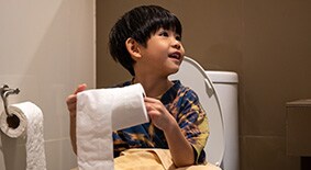 Little boy sitting on toilet holding toilet paper roll