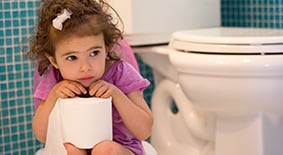 Toddler girl sitting in bathroom holding roll of toilet paper