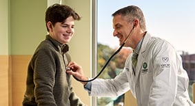 A heart doctor smiling as he listens to a teenager's heartbeat.