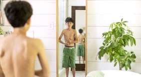 preteen boy looking at body in mirror