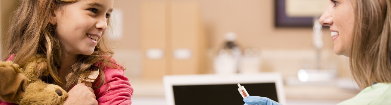 young girl holding teddy bear while getting flu shot