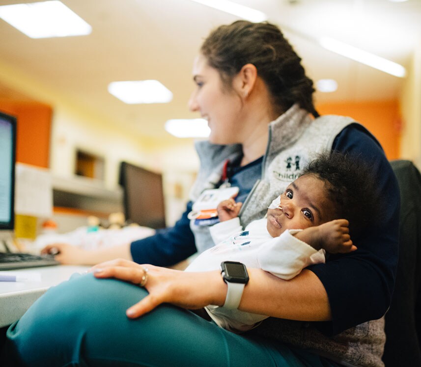 pediatric nurse cradles infant patient at nurse's station