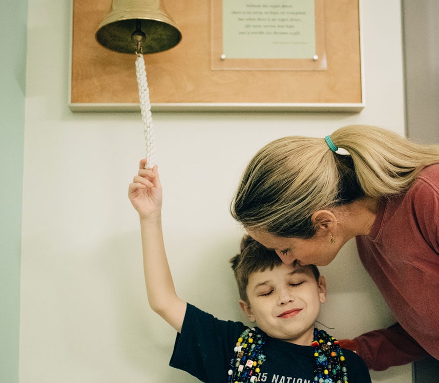 Young boy ringing bell at pediatric hospital marking the end of cancer treatment