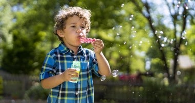 toddler boy blowing bubbles in yard