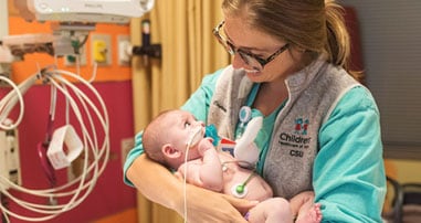 nurse holding baby over crib in hospital room