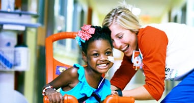 nurse laughing with girl on bike in hospital hallway