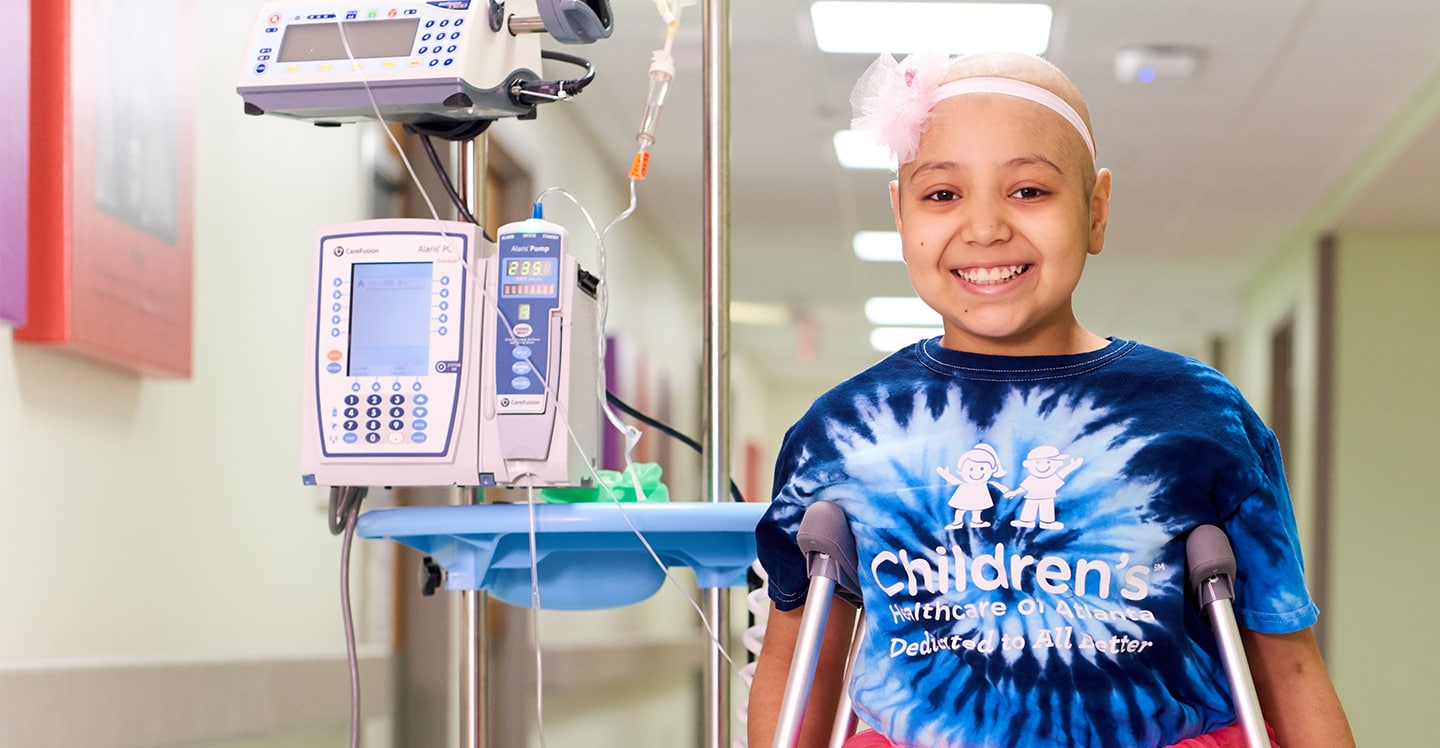 Pediatric cancer patient wearing a tutu smiles in hospital hallway
